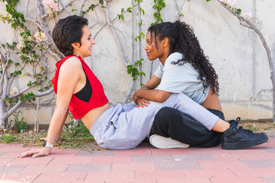 Side view of content multiracial girlfriends in casual wear looking at each other while having conversation near building on street