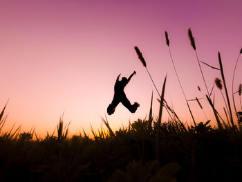 Silhouette man jumping on field against sky during sunset