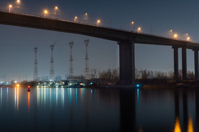 Illuminated bridge over river against sky at night