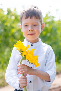 A cute boy in a field of sunflowers in a white shirt stands and smiles.