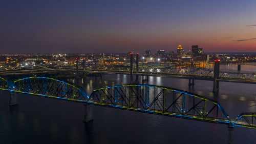 Illuminated bridge over river against buildings in city at night