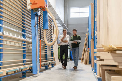 Two carpenters walking and talking amid wooden planks in production hall