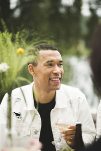 Smiling young man looking away while holding wineglass during dinner party