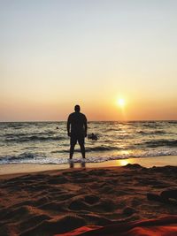 Rear view of silhouette man on beach against sky during sunset