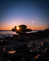Silhouette rock on beach against sky during sunset