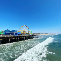 Santa monica pier amusement park by sea against clear blue sky