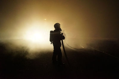 Silhouette man photographing on illuminated road at night