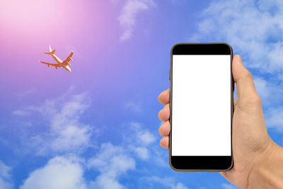 Cropped hand of person holding mobile phone against airplane