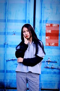 Portrait of beautiful woman standing against blue metal