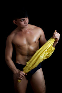 Shirtless young man holding plastic bag while standing against black background