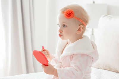 Cute girl applying make-up while sitting on bed at home