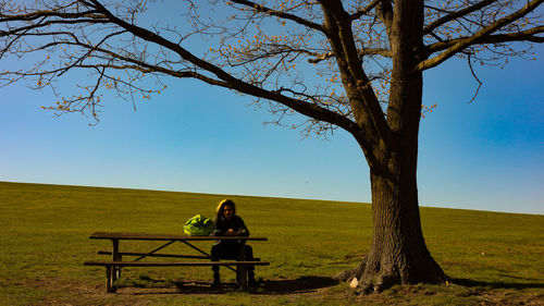 People sitting on bench on field against sky