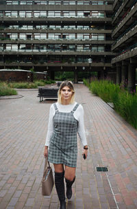 Portrait of smiling young woman walking on footpath against building