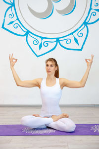 One woman is doing lotus posture with her hands up and om sign