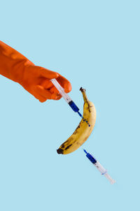 Cropped image of hand injecting banana against blue background