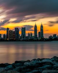 Sea by buildings against sky during sunset