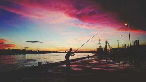 Silhouette man fishing in sea against sky during sunset