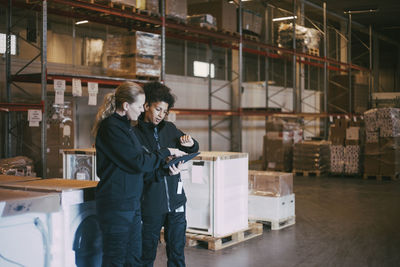 Female colleagues discussing over digital tablet at logistics warehouse