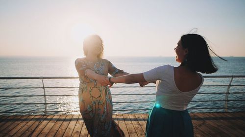 Women standing at beach against sky during sunset