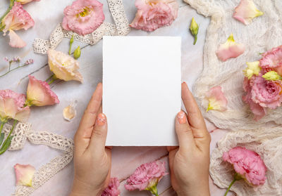 Hands holding a blank card over a marble table decorated with flowers and ribbons