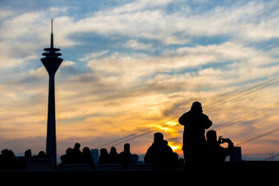 Silhouette people by rheinturm tower during sunset in city