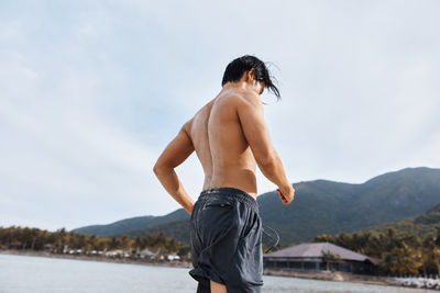 Rear view of shirtless man standing against lake