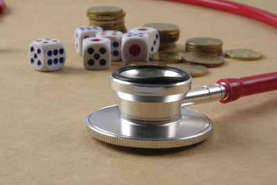 Close-up of stethoscope with dices and coins on brown table