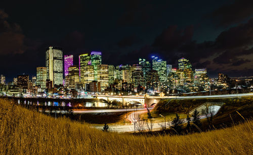 Illuminated buildings by river against sky in city at night