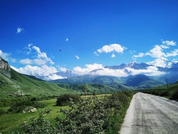 Road leading towards mountains against blue sky