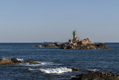 Lighthouse by sea against clear sky