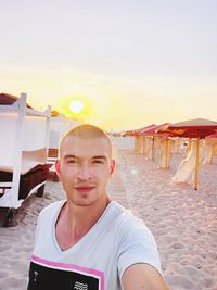 Portrait of young man on beach against sky during sunset