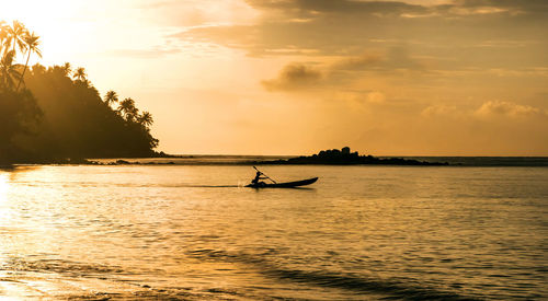 Silhouette man rowing boat in sea against sky during sunset