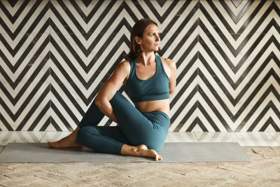 Full length of woman exercising while sitting on floor against wall