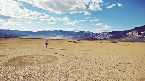 Rear view of man walking at desert against mountains