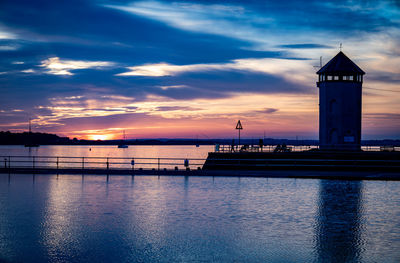 Lighthouse by sea against sky during sunset