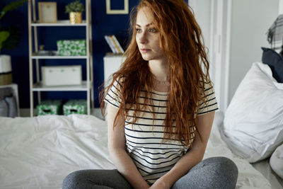 Portrait of young woman sitting on bed at home