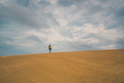 Rear view of man with backpack walking on sand dune in desert