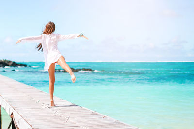 Woman with arms outstretched on beach against sky