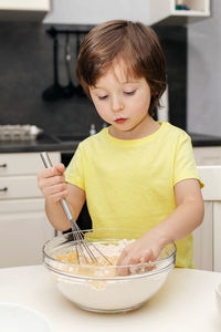 Little boy kneading dough with a whisk in the kitchen and smiling. time with children at home. 