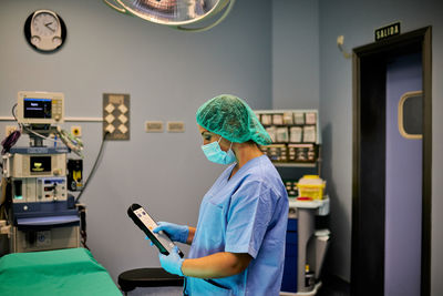 Unrecognizable medical specialist in uniform and gloves adjusting hospital bed by using remote control during duty in modern equipped ward