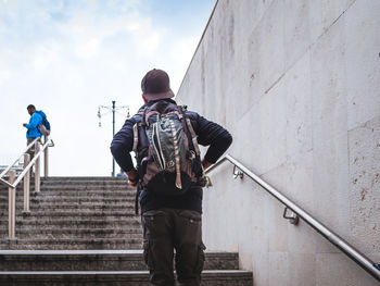 Rear view of man holding umbrella on staircase against sky