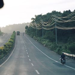 People riding bicycle on country road against sky