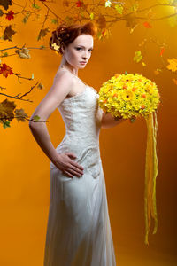 Portrait of beautiful bride holding bouquet while standing against orange background