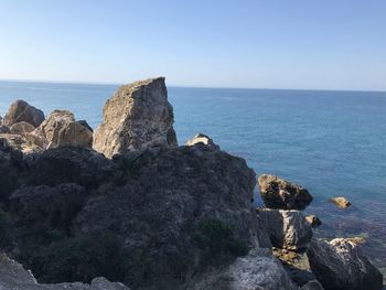 Rock formations by sea against clear blue sky