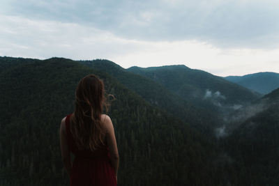 Rear view of woman standing on mountain against sky