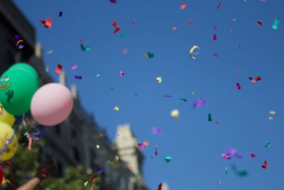 Low angle view of balloons and confetti against clear blue sky