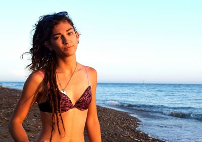 Portrait of seductive woman standing on beach against clear sky