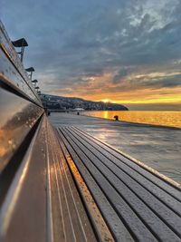 Bench by sea against sky during sunset