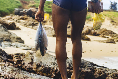 Low section of man standing on rock at beach