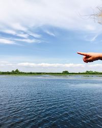 Cropped hand pointing over lake against sky
